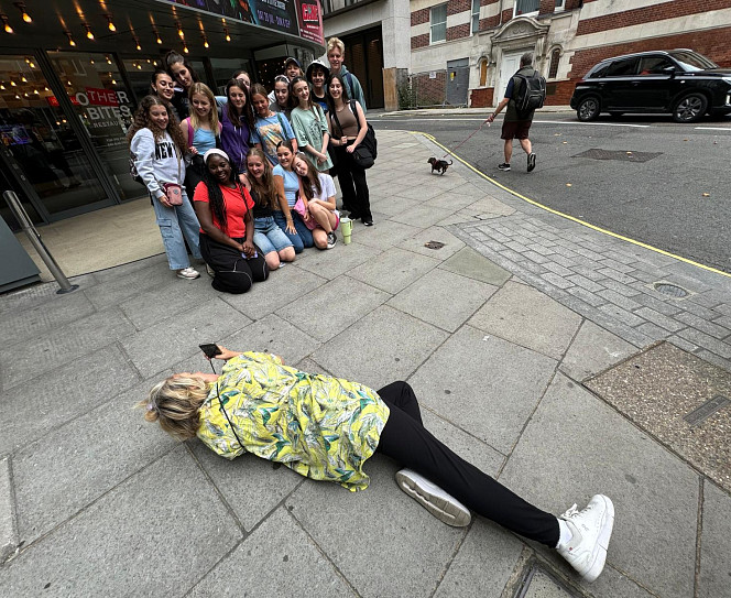 The crescendo company having their photo taken in front of The Other Palace theatre, with the photographer lying on the floor in front of them.